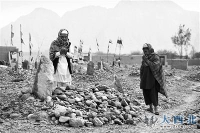 　　24日，阿富汗坎大哈省，两名当地村民在堆满石块的坟前为枪击案遇害者祈祷。