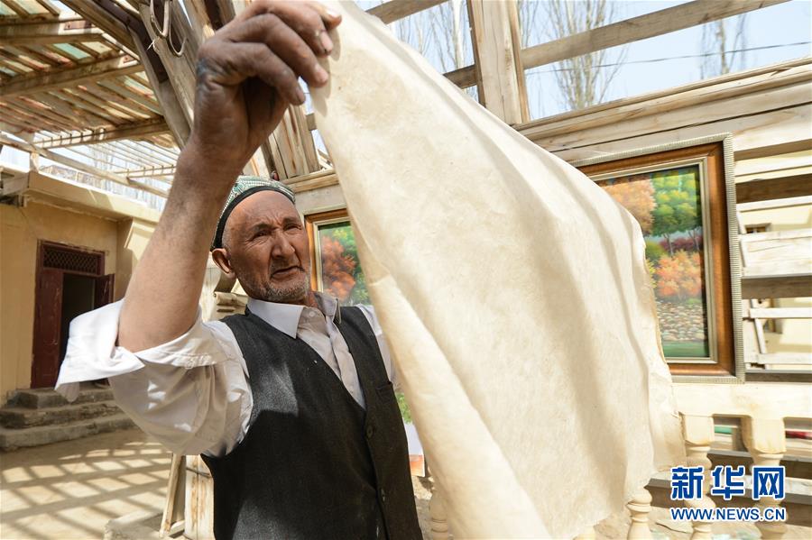 来自新疆和田地区墨玉县扎瓦镇库木艾日克村的“农民画家”阿卜力克木·麦麦提敏在家中挑选手工制作的桑皮纸,准备进行油画创作(2019年3月5日摄)。